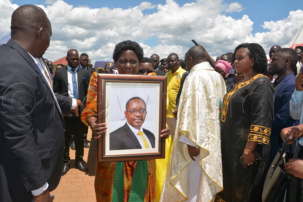 Janipher Namuyangu, the Minister of State for Bunyoro Affairs, holding a portrait of the deceased Banura and other leaders as they received his remains. (Credit: Peter Abaanabasazi)