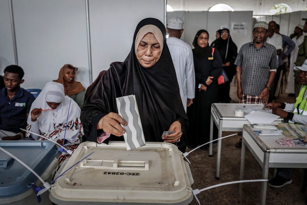 A voter casts her ballot while others queue at the Maundi voting centre in Stone Town on October 29, 2025, during Tanzania's presidential elections. (Credit: AFP)