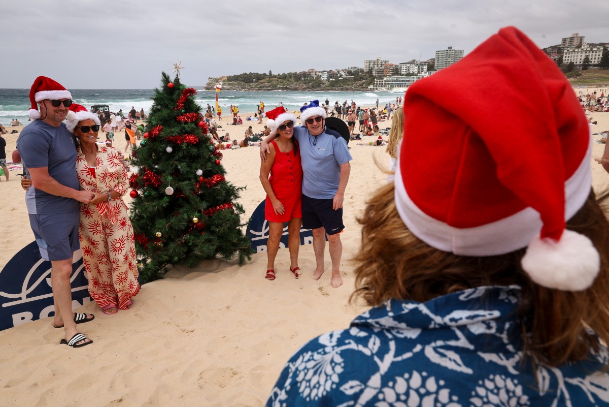 Tourists wearing Christmas costumes pose in front of a Christmas tree on the sand at Bondi Beach in Sydney on December 25, 2025. 