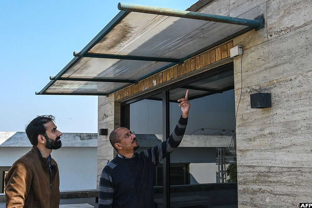 Umair Shahid (R) and Taha Ali, academics and founders of Curious Friends of Clean Air (CFCA), pointing at an air-quality measuring device at their office in Islamabad