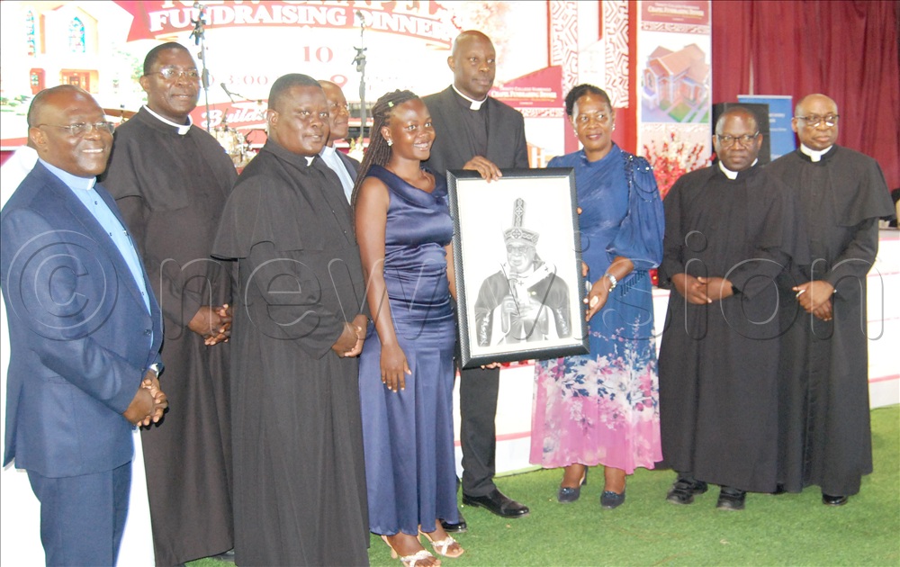 The headteacher of Trinity College Nabbingo, Immaculate Lwanga (third-right), and the Catholic clerics including Msgr. Rogers Kabuye (fifth-left), Fr. Dr. Mark Richard Ssajjabbi (left), Fr. Mathias Wamala (second-left), Fr. Dr. Ambrose Bwangatto (third-left), Fr. Johh Chrysostom Kiwanuka (second-right), and Fr. Dr. Nicholas Kiruma (right) posing for a photo with the portrait of Archbishop Paul Ssemogerere that was auctioned during the fundraising dinner for the new chapel of Trinity College Nabbingo. The function took place at the school's sports ground on Masaka Road, in Wakiso district on Saturday, October 10, 2026.