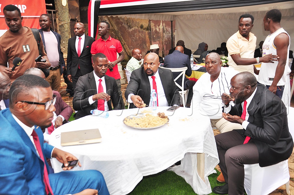 The CMP secretary general Moses Bigirwa and party president, Mubarak Munyagwa eating pilao on a platter, a party symbol for resource sharing as other party members look on. (Photo by Isaac Nuwagaba)