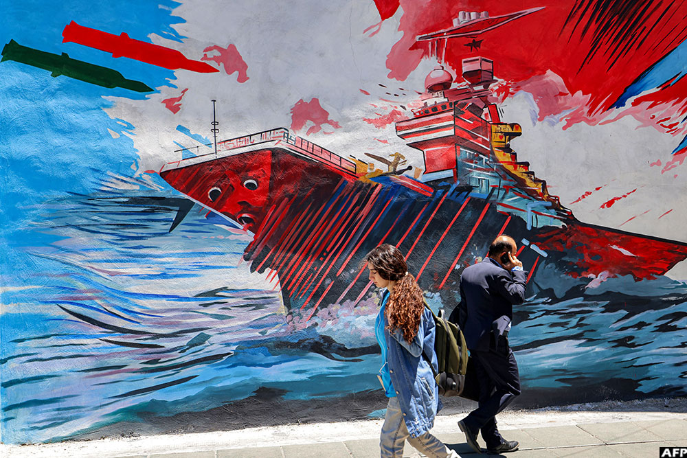People walk past an anti-US and anti-Israel mural depicting missiles hitting an aircraft carrier in Tehran on May 26, 2026