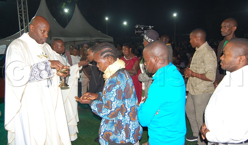 The Vicar-General of Kampala Archdiocese, Msgr. Rogers Kabuye distributing Holy Communion during the New Year's Eve mass at YES Centre Sports Arena, Nsambya, in Makindye Division. (Photo by Mathias Mazinga)