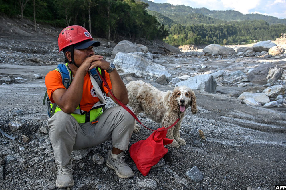 A search and rescue team member, along with a sniffer dog, sits on the banks of the Trishuli River as they look for missing people following the August 26 flash flood in Nepal's Nuwakot district on September 30, 2026.
