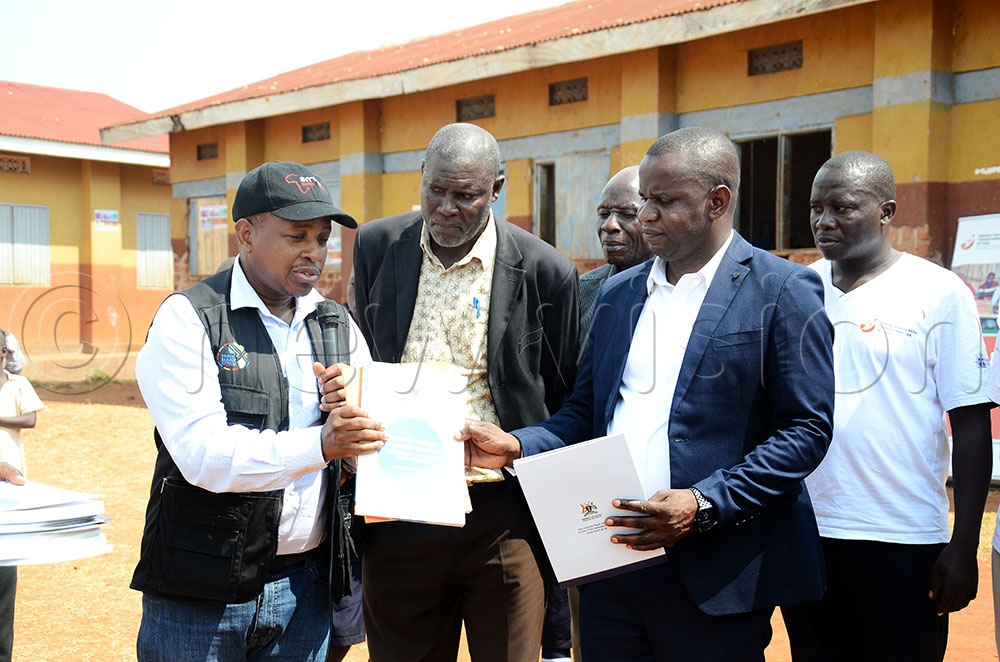 (L-R) Dr Patrick Kagurusi the Amref Health Africa Uganda Country Manager hands over copies of school health training manuals from ministry of health to Fred Muwubani the Mayuge District Inspector of Schools and David Ziija the Mayuge District Chairperson. This was during the commissioning of a 10,000-litre capacity water tank at Lwanika Modern Primary School in Bukatube sub county Mayuge district on June 30, 2026. (Credit: Lawrence Mulondo)