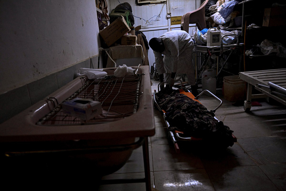 This photo taken on April 18, 2026 shows Sudanese Ali Gebbai, a volunteer responsible for handling burial procedures for unidentified bodies in the capital, Khartoum, examines one of the unidentified corpses at the mortuary of Omdurman's Al-Nao Educational Hospital. 