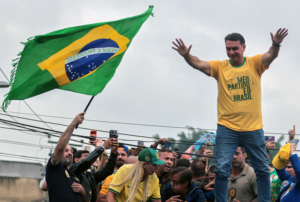 Brazil's right-wing senator and presidential candidate Flavio Bolsonaro of the Liberal Party (PL) gestures as the candidate for state deputy Ralph Gracie (L) waves a national flag during a campaign rally on the eve of the general election, in Campo Grande neighbourhood, in the western zone of Rio de Janeiro, Brazil on October 3, 2026. (Photo by Douglas SHINEIDR / AFP)
