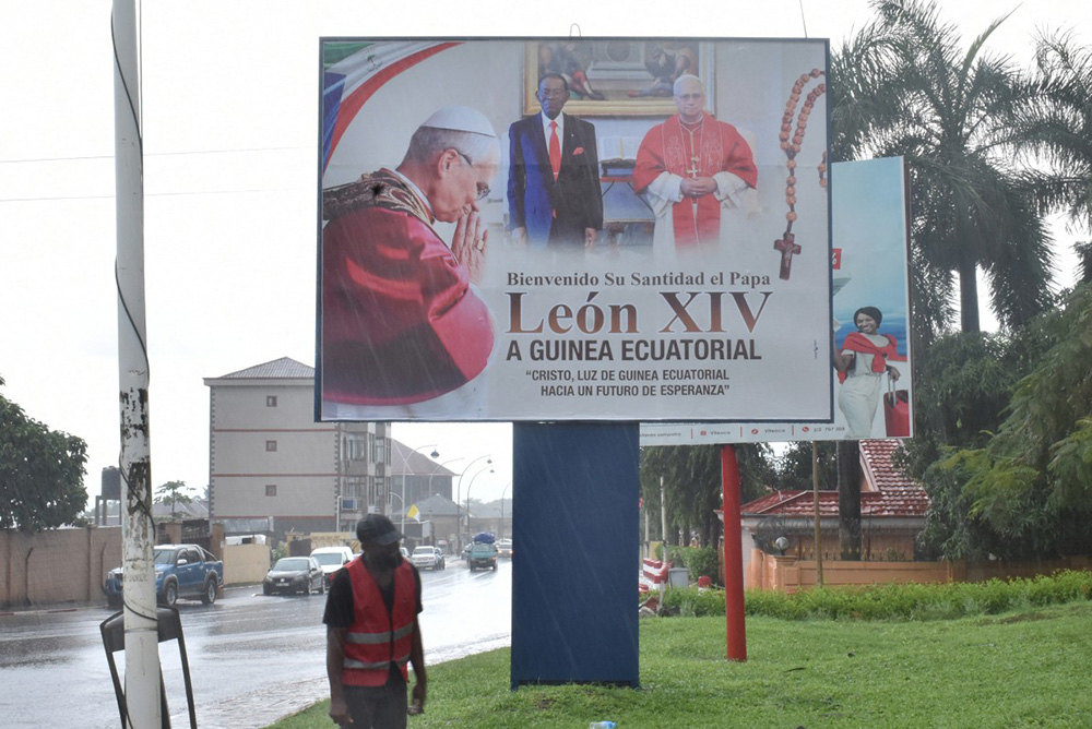 A man walks next to a billboard displaying a portrait of Pope Leo XIV (L and R) and Guinea Equatorial President, Teodoro Obiang (C), in Malabo on April 15, 2026 ahead of the Pope's visit to Equatorial Guinea. (Photo by Samuel Obiang / AFP)