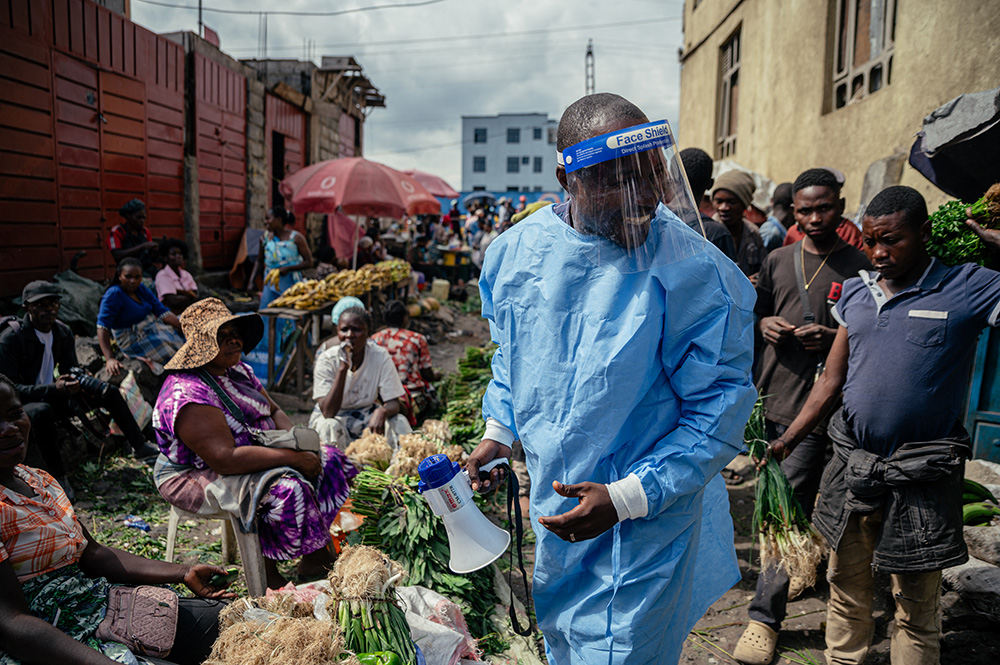 Cousin Kasumbo, president of the U Report Goma community, dressed in protective equipment, raises awareness among traders alongside young members of the “U Report Goma” group who continue awareness activities at Alanine market using megaphones and focus group discussions as part of Ebola prevention and awareness measures in Goma, on May 29, 2026. (Photo by Jospin Mwisha / AFP)