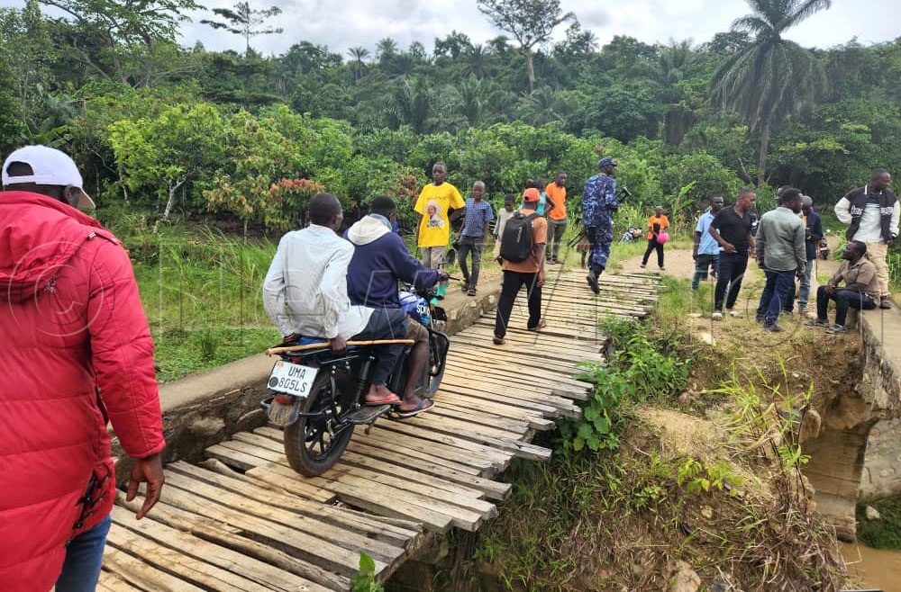 Residents using a temporary wooden bridge that they put over the collapsed Tokwe Bridge in Bundyelume Village, Tokwe Sub-county Bundibugyo district. The bridge was constructed with sh350 without steel reinforcement. This was during Balaam Barugahara the Local Government Minister visit to the district to investigate alleged corruption and abuse of public resources under the government’s anti-corruption campaign, Expose the Corrupt’ on August 22, 2026. (Credit: Lawrence Mulondo)