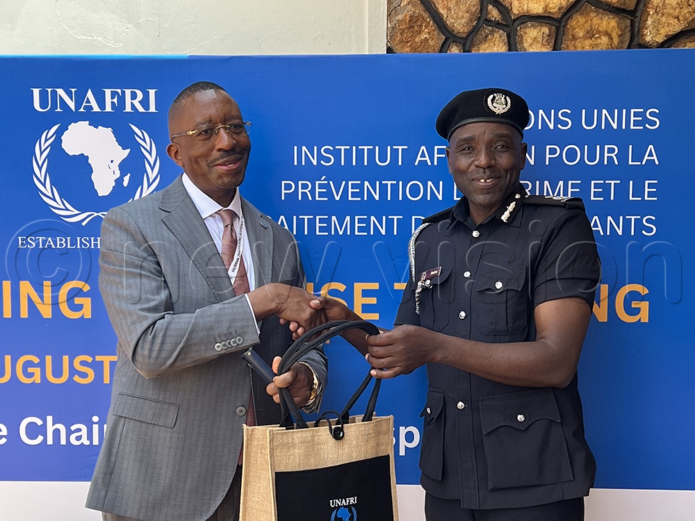 UNAFRI Acting Director General Andrew Munanura Karokora handing over a gift to Assistant Commissioner of Police Ramathan Doka dressed in black police uniform.