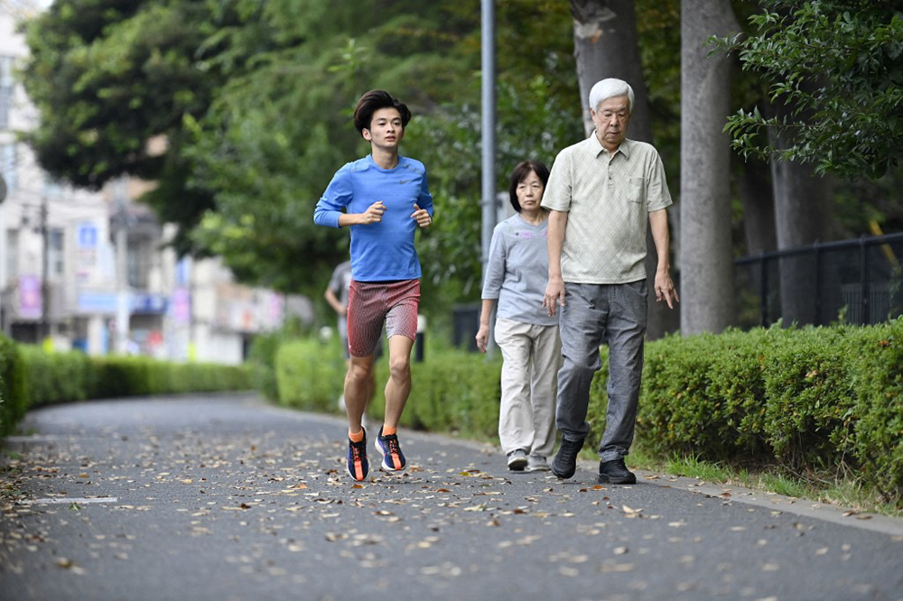  A young man runs past an elderly couple taking a health walk early in the morning on October 1, 2024, in Tokyo, Japan.