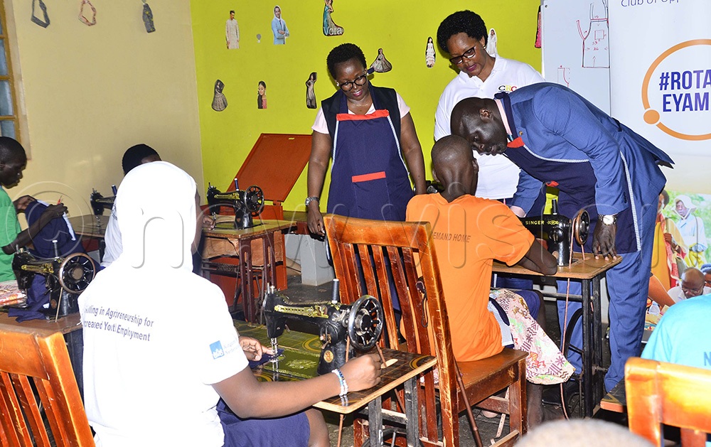 Gerald Obai, District Governor for District 9213, interacts with one of the girls doing tailoring at the Remand Home, as Elizabeth Mushabe, Rotary Club of Upper Kololo president, and Mary Kyomugisha, Naguru Remand Home in charge look on during the courtesy visit at Naguru Remand Home in Kampala on 14th August 2026. (Photo by Juliet Kasirye)