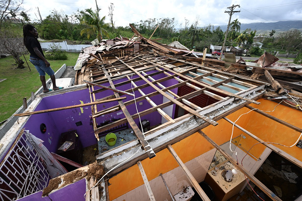 A man stands on what is left of the roof of his neighbor following the passage of Hurricane Melissa, in longwood, St Elizabeth, Jamaica on October 29, 2025. (AFP)