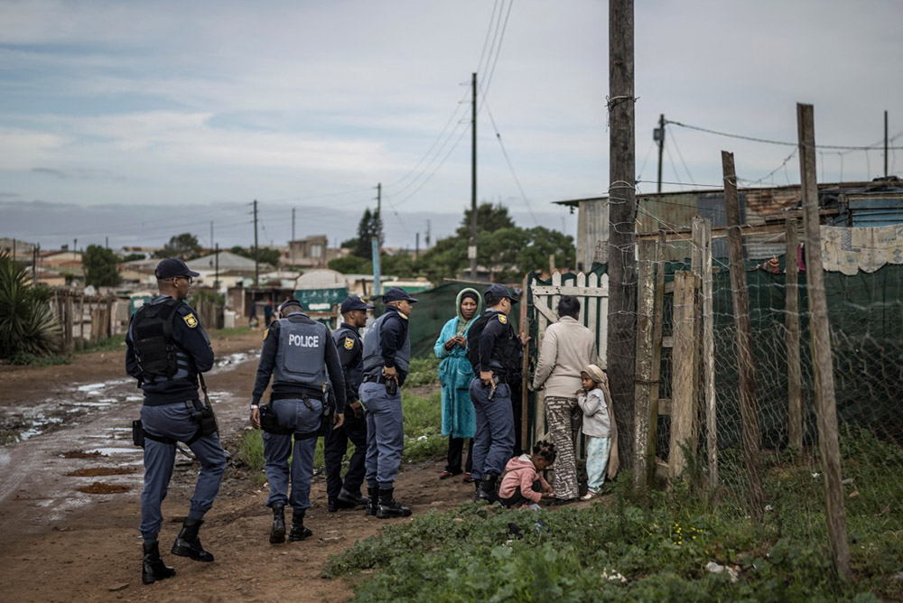 South African Police Service officers hold their hands on their holstered weapons as they conduct a search on the premises of residents suspected of harbouring looted items in the Pellsrus township in Jeffreys Bay, on July 18, 2026. (Credit: AFP)