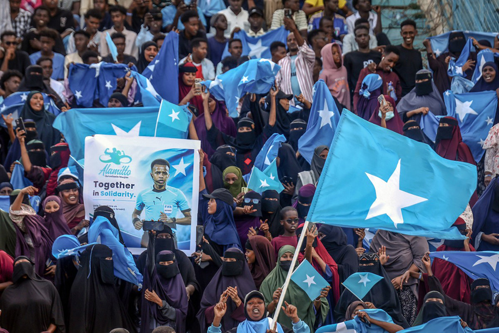 Supporters of Somali international referee Omar Abdulkadir Artan hold flags and banners as they welcome him ahead of a solidarity football match after his return to Somalia in Mogadishu on June 10, 2026. (Photo by Hassan Ali Elmi / AFP)