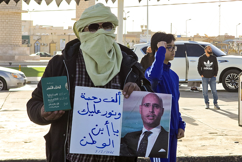 A man holds the "The Green Book" and the image of the late Seif al-Islam Gaddafi, the son of Libya's late longtime ruler, prior to the funeral in Bani Walid, in the Tripoli region, western Libya on February 6, 2026. (AFP)