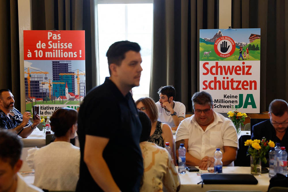 A man walks past election placards reading "Not a 10-million Switzerland" (L) and "Protect Switzerland" as the Swiss vote on a divisive anti-immigration proposal to cap the country's population and another referendum on restricting access to conscientious objection to military service, in Aarberg on June 14, 2026. (Credit: AFP)