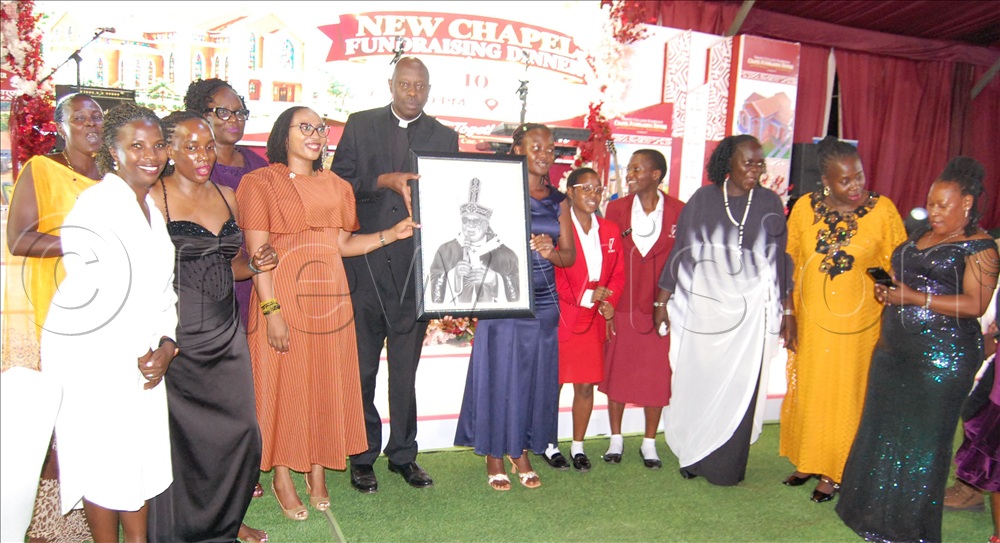 The Vicar-General of Kampala Archdiocese, Msgr. Rogers Kabuye Mukasa (wearing a clerical shirt) presents the portrait of archbishop Paul Ssemogerere to the members of TRICONA's Alexi House who were the highest bidders. This was durng the fundraising dinner for Trinity College Nabbingo's new chapel at the school's sports ground on Masaka Road, in Wakiso district on Saturday, October 10, 2026.