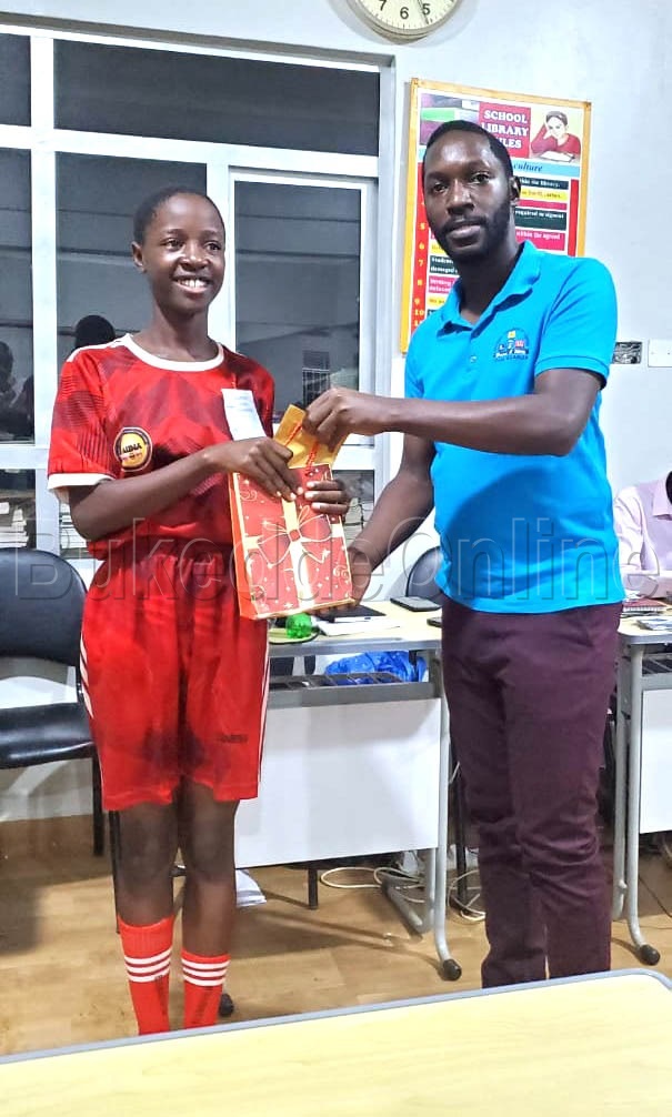 Amyuka akulira eby'ekikugu mu kibiina ekitwala omuzannyo gwa Scrabble mu Uganda Godwin Murungi ng'akwasa omuzannyi akize ku banne ensimbi ssaako ne board ya Scrabble ku mutendera gw'amasomero ga  Primary 