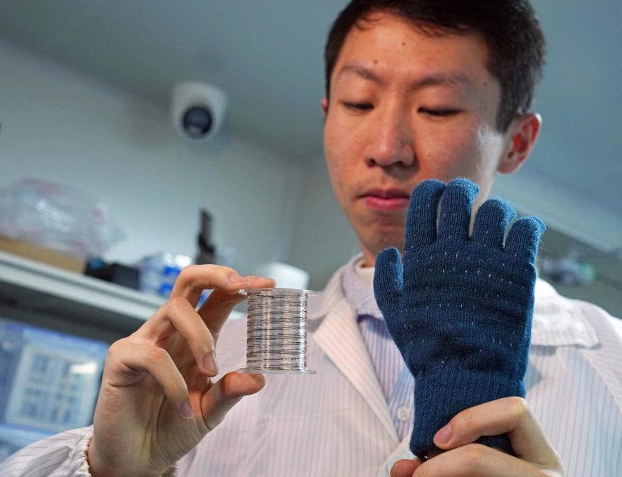 A researcher displays rolled-up "fiber chips" and a smart tactile glove made by weaving the chips into textiles at Fudan University in east China's Shanghai, Jan. 19, 2026. (Xinhua/Liu Ying)