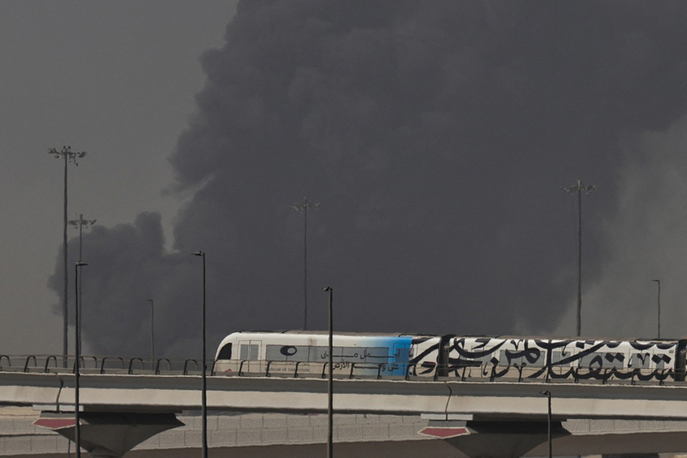 A metro train passes a plume of smoke rising from the port of Jebel Ali following a reported Iranian strike in Dubai on March 1, 2026. (AFP)