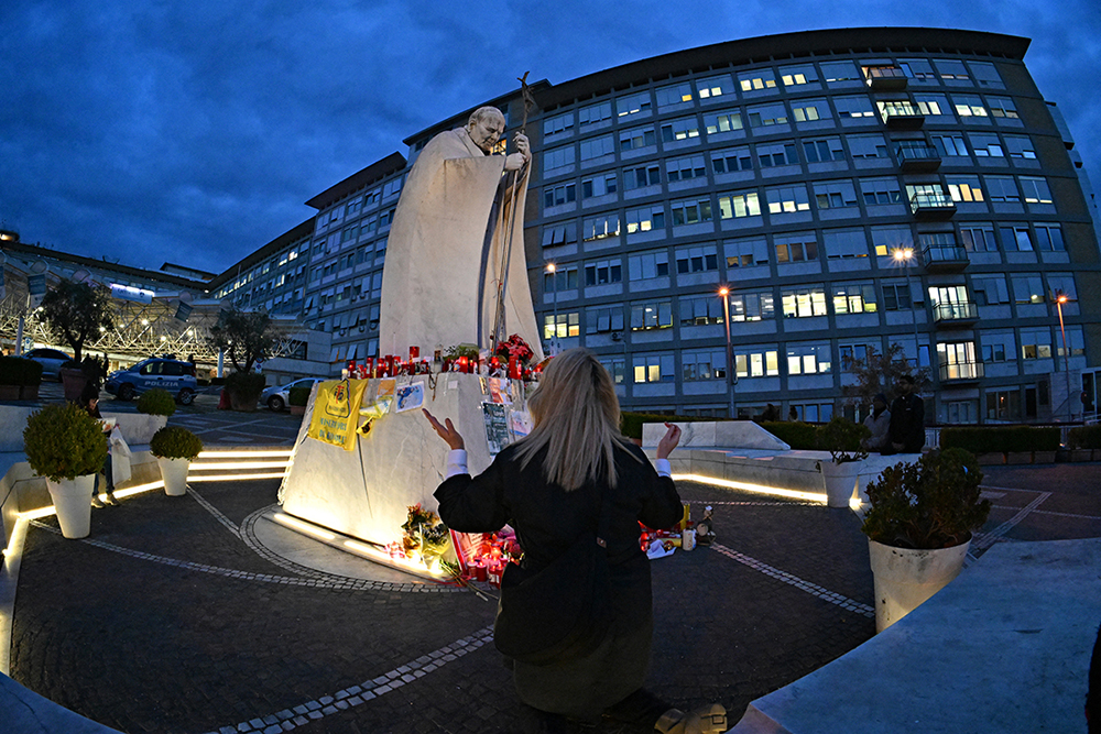 A woman prays at the statue of John Paul II outside the Gemelli University Hospital where Pope Francis is hospitalized with pneumonia, in Rome on March 9, 2025 (AFP Photo)