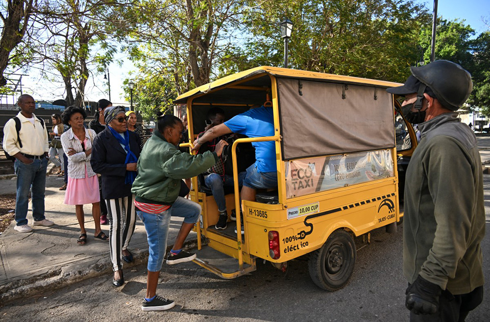 People line up to board an electric tricycle on a street in Havana, on February 13, 2026. The fuel crisis in Cuba, and particularly in Havana, is forcing many workers who depend on daily mobility to abandon gasoline cars and turn to electric tricycles and bicycle taxis as more accessible alternatives. (Photo by YAMIL LAGE / AFP)