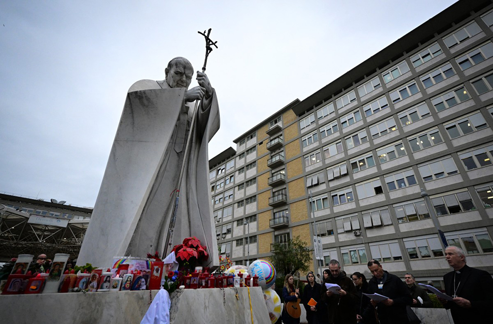 People pray at the statue of John Paul II outside the Gemelli hospital where Pope Francis is hospitalized in Rome on February 24, 2025. (AFP)