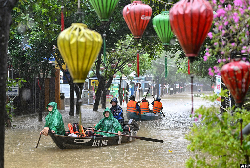 People navigate a flooded street on boats during heavy rains in Hoi An on October 30, 2025