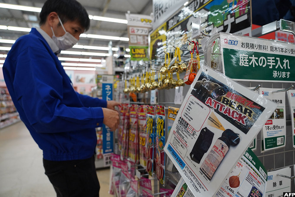 A staff member sorts bells next to an advertisement for bear spray at a store in Hanamaki, Iwate prefecture.