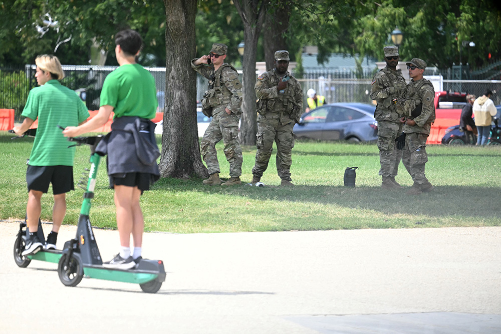People ride scooters past members of the US National Guard on the National Mall in Washington, DC, on August 14, 2025.  (Photo by Jim WATSON / AFP)