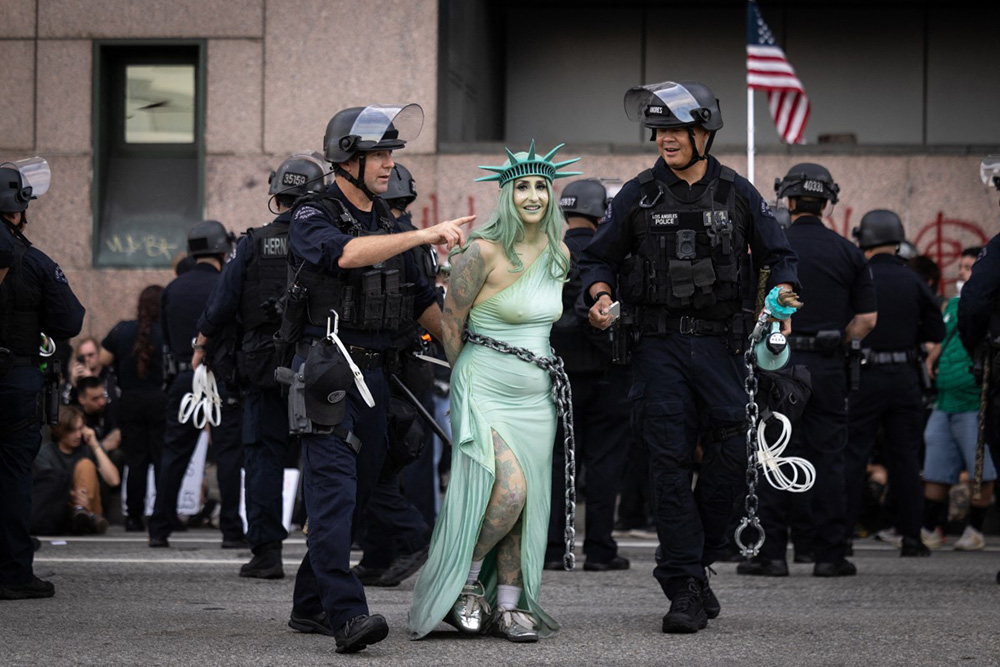 LAPD officers arrest a protester dressed as Lady Liberty in chains following clashes near the Metropolitan Detention Center during the "No Kings" national day of protest in Los Angeles on March 28, 2026. (Photo by ETIENNE LAURENT / AFP)