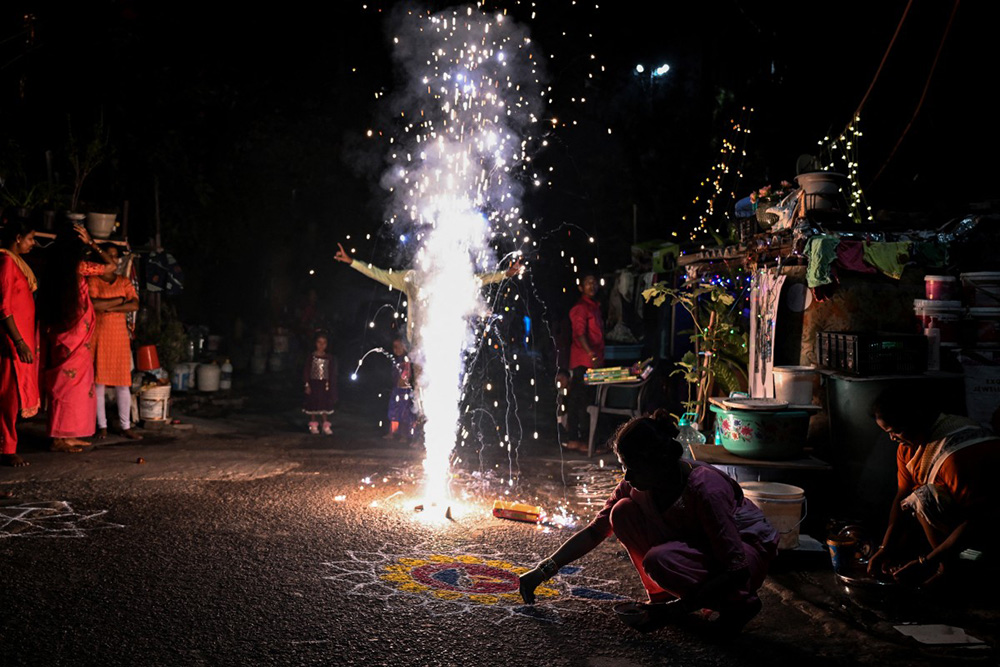Revellers light fireworks as others prepare a ravioli during the celebrations to mark Diwali, the Hindu festival of lights, in New Delhi on October 20, 2025. (Photo by Sajjad  HUSSAIN / AFP)