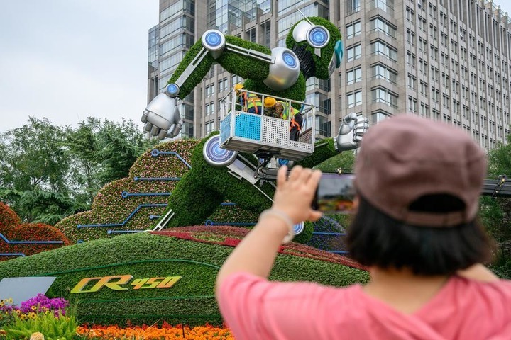 A woman takes pictures of a set of floral decorations under construction at Dongdan area along Chang'an Avenue in Beijing, capital of China, Sept. 25, 2026. Floral decorations have been set up along the Chang'an Avenue in Beijing ahead of China's National Day holidays. (Xinhua)
