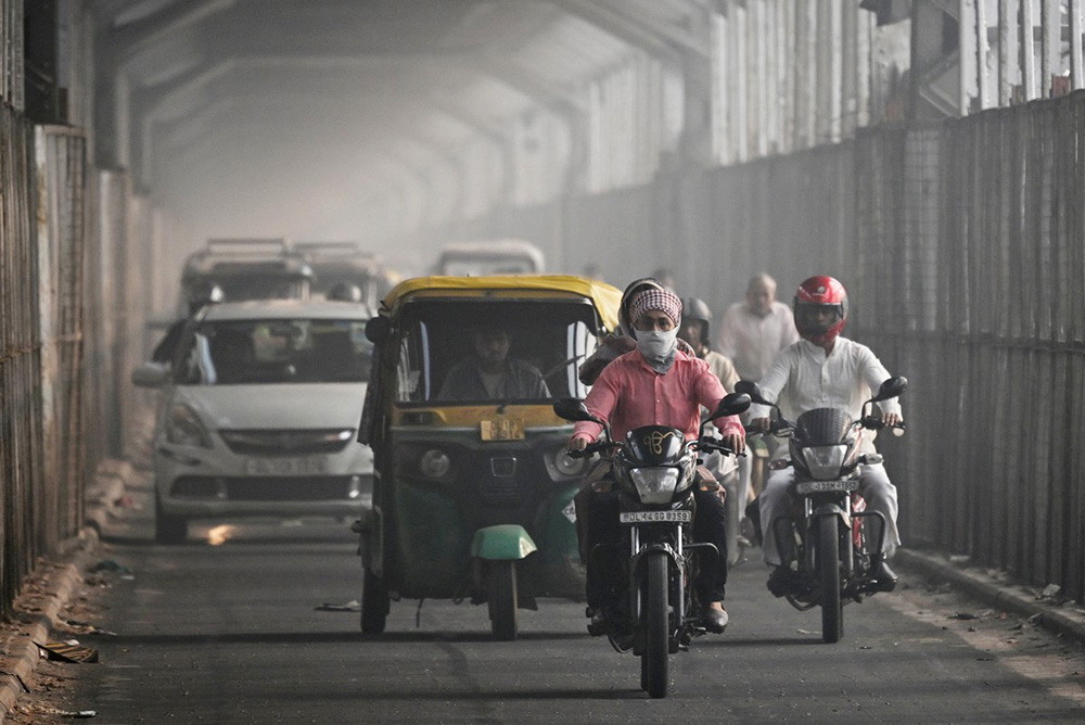 A commuter with his face covered in cloth rides along a bridge across river Yamuna in New Delhi on October 21, 2025, as smog engulfed the city skyline a day after Diwali, the Hindu festival of lights. (Photo by Arun SANKAR / AFP)