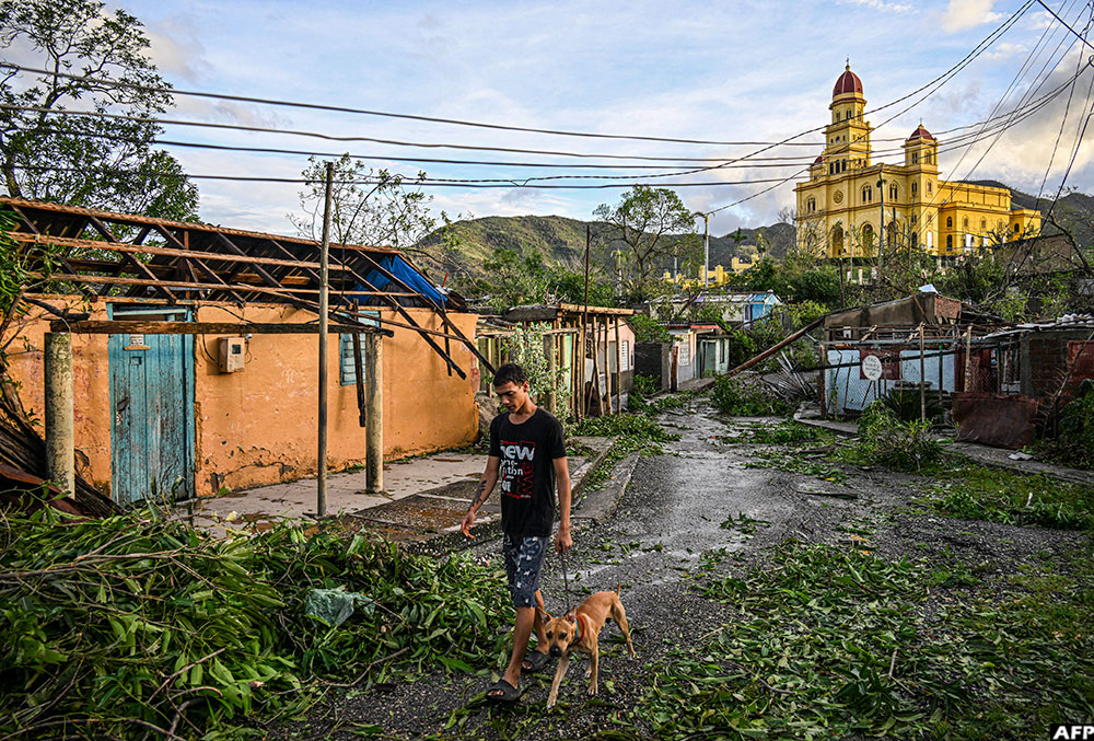 A resident of El Cobre, in the city of Santiago de Cuba, walks his dog past downed trees, power lines and destroyed houses following the passage of Hurricane Melissa