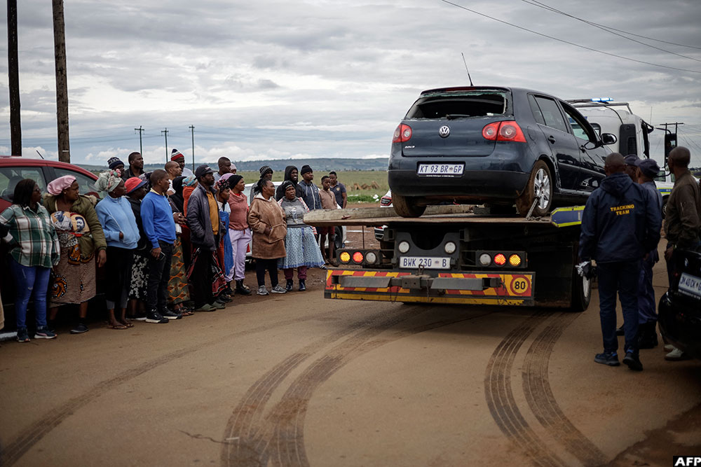 A vehicle with a broken back window is taken away by a South African Police Service (SAPS) vehicle at the scene of Sunday's deadly attack
