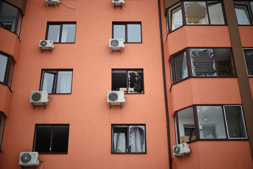 A local resident removes glass shards from a broken window in a residential buidling following an air attack in Sofiivska Borshchagivka, Kyiv region on February 22, 2026, amid the Russian invasion of Ukraine. (Photo by Henry NICHOLLS / AFP)