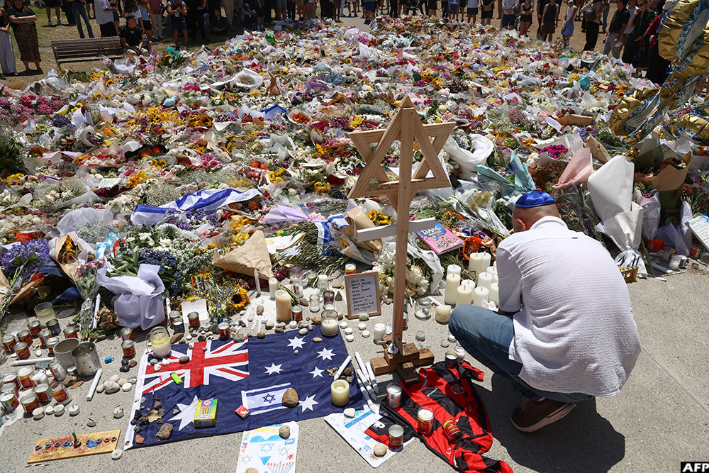 A mourner lights candles as people gather around floral tributes outside Bondi Pavilion in Sydney on December 17, 2025, to honour victims of the Bondi Beach shooting
