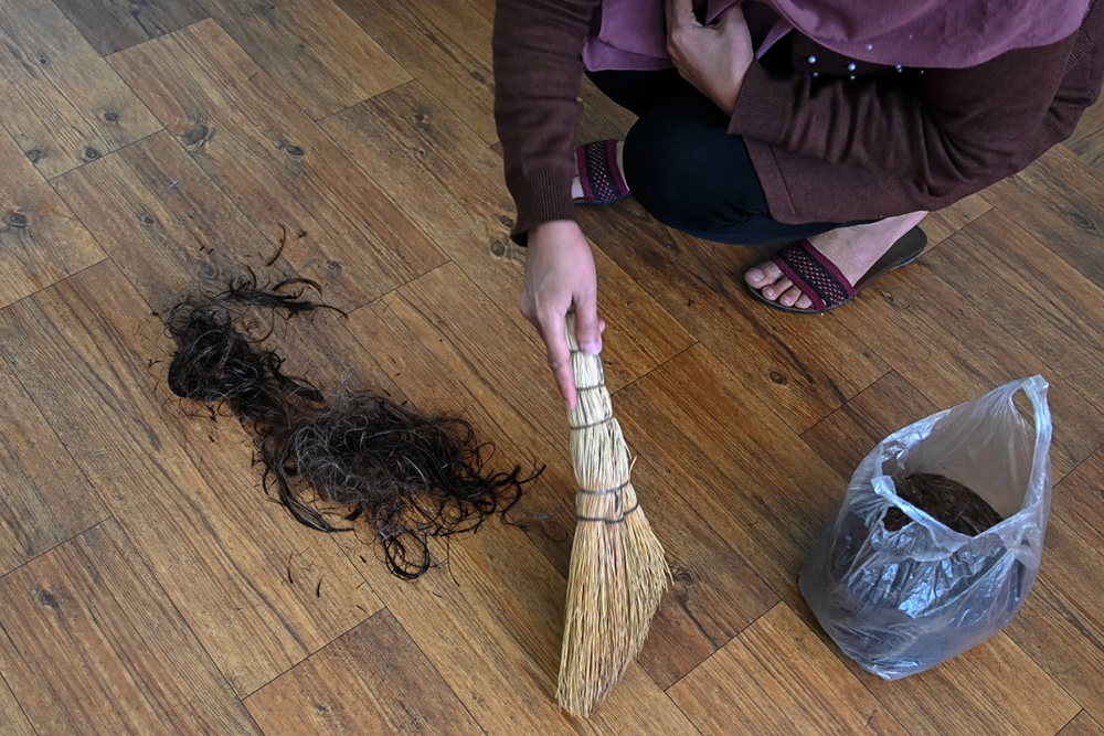 An Afghan woman hairdresser collecting hair left on the floor after giving a haircut to a client at a salon in Kabul. (AFP Photo)