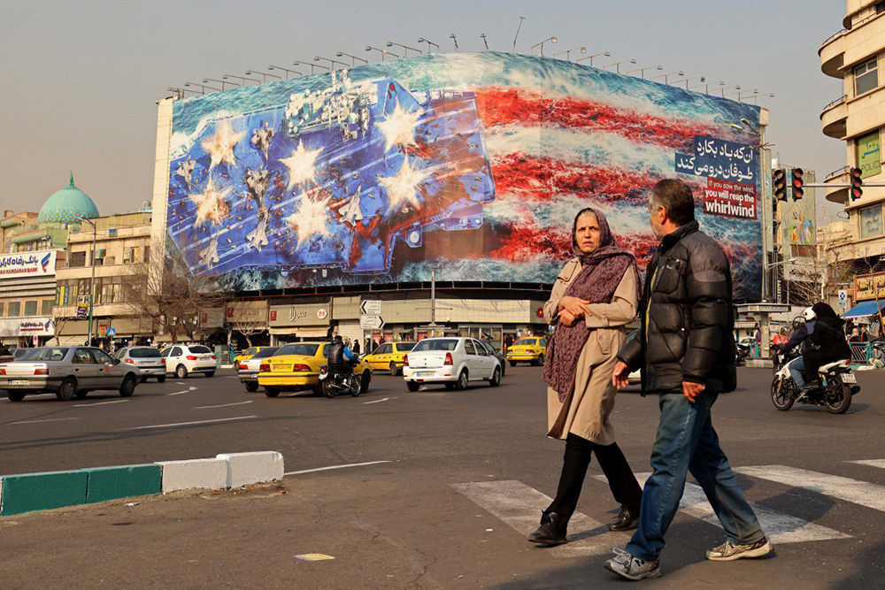 Commuters walk past an anti-US billboard installed on a building at the Enqelab Square in Tehran on January 26, 2026. (Photo by ATTA KENARE / AFP)