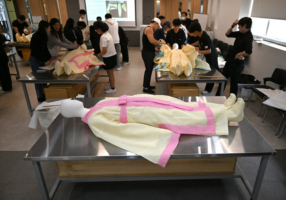 In a photo taken on September 24, 2025, students drape a mannequin in traditional Korean funeral cloth during a funeral administration class at the Busan Institute of Science and Technology in Busan. 