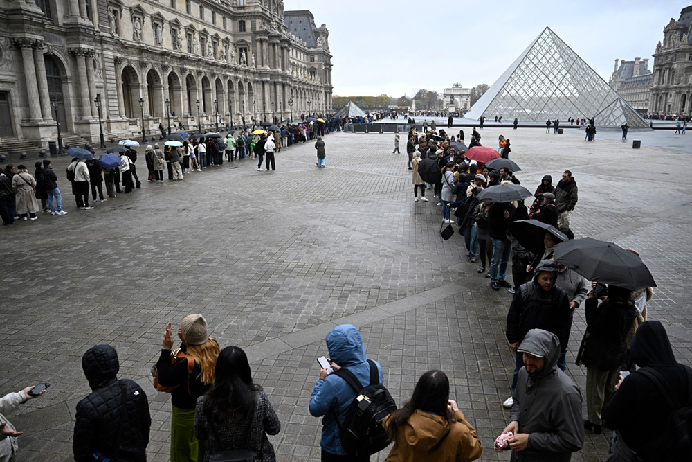 People queue in the Louvre pyramid courtyard moments before the announcement the museum will remain closed for a second day running after thieves stole crown jewels from the museum in Paris a day earlier, in Paris on October 20, 2025.