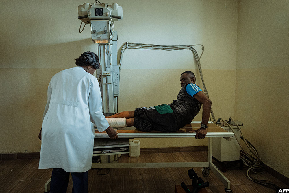 Elise Nzuzi, an A1-level radiology technician, positions a patient on the X-ray table before reviewing the control image on the lightbox at the Shirika la Umoja centre in Goma