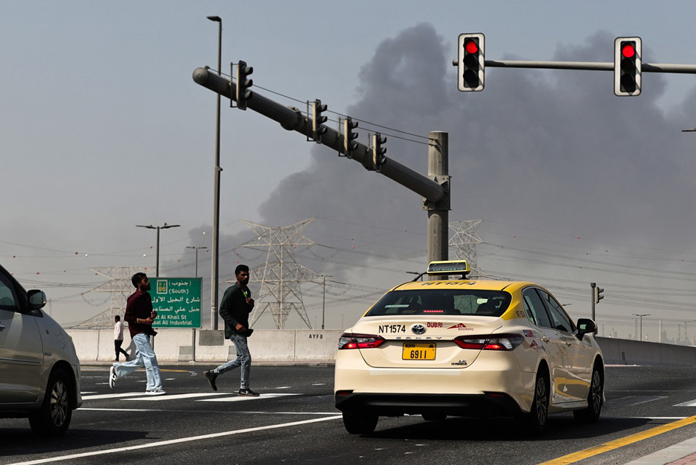 People cross a street as smoke rises from the site of a reported Iranian strike in Dubai on March 1, 2026. (AFP)