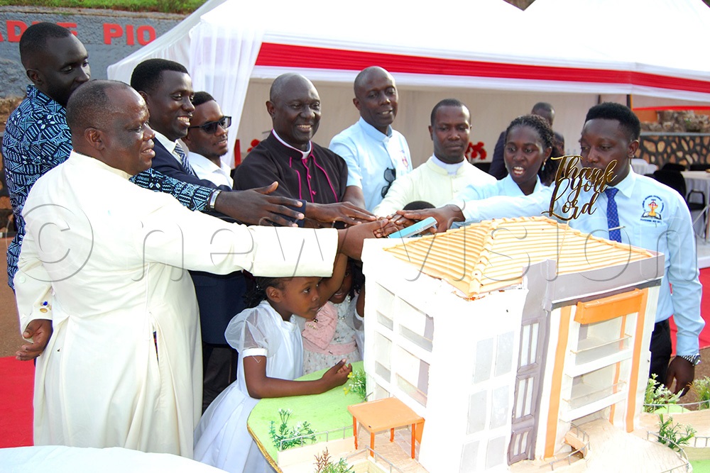 Msgr. Dr. Laarry Ssemusu (wearing a black cassock) is joined by Fr. Joseph Kirumira (left) and some members of the Pastoral Council of St. Charles Lwanga Catholic Community, MUBS, as he cuts cake in celebration of his 45th priestly anniversary and 70th birth-day at MUBS on Saturday, October 4, 2025. (Photo by Mathias Mazinga)