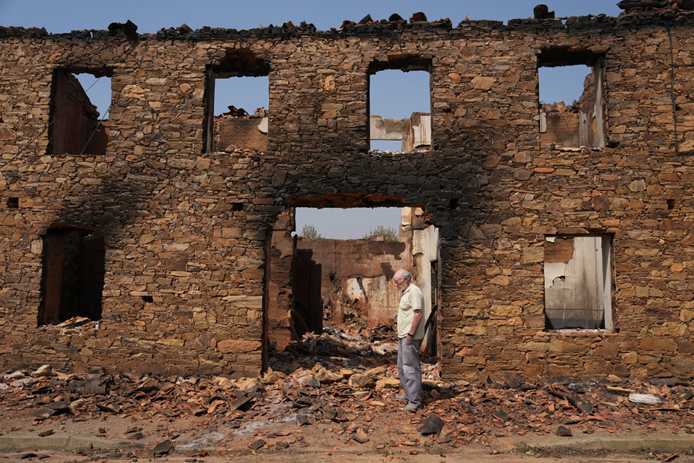A man stands in front of a burnt house in ruins after a wildfire in the village of Castrocalbon, northwestern Spain, on August 16, 2025. Spain, now in its third week under a heatwave alert, is still battling wildfires raging in the northwest and west of the country, where the army has been deployed to help contain the blazes. The regions of Castilla y Leon, Galicia, Asturias and Extremadura remain the hardest hit. 