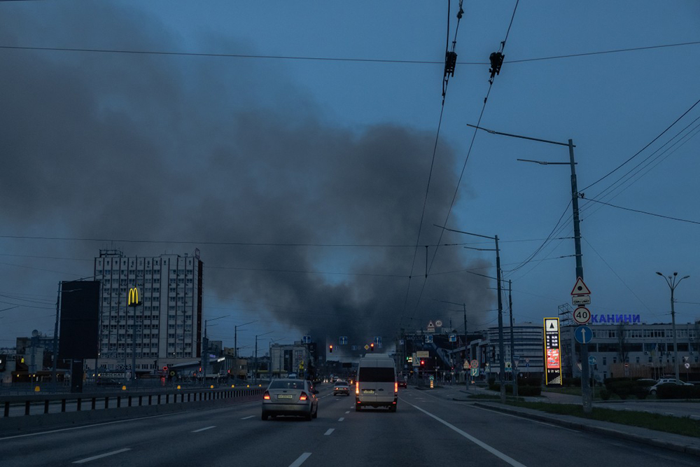 Cars drive on a road as smoke rises in the distance, following the Russian missile attack, in Kyiv on April 6, 2025, amid the Russian invasion of Ukraine.